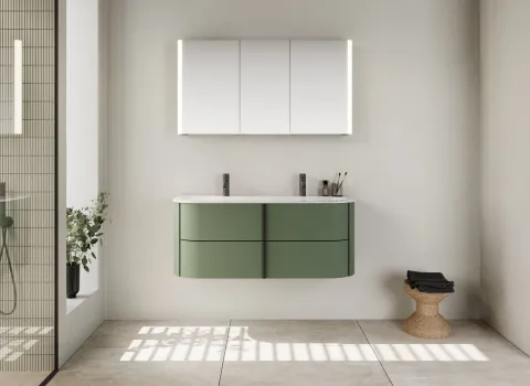 Ein Badezimmer mit einem hängenden Waschtisch aus der Burgbad Lavo 2.0 Serie in grünem Finish, ausgestattet mit zwei Wasserhähnen und einer weißen Waschtischplatte.