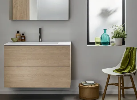 Modernes Stocco Badmöbel mit heller Holzfront, weißem Waschtisch und wohnlichen Accessoires am Fenster.