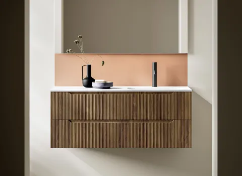 Stocco Badmöbel mit geriffelter Holzfront vor terrakottafarbener Wand und minimalistischem Spiegel.